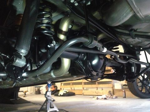 2013 Ford Mustang - The rear suspension and drivetrain components of a vehicle are visible from underneath, supported by jack stands.