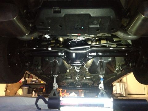 2013 Ford Mustang - The undercarriage of a vehicle is visible, supported by jack stands, with a bright work light illuminating the scene.