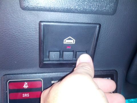 1989 BMW 3 Series - A finger presses a button on a car's interior control panel, which includes labels for 'SRS' and 'BRAKE OIL'.