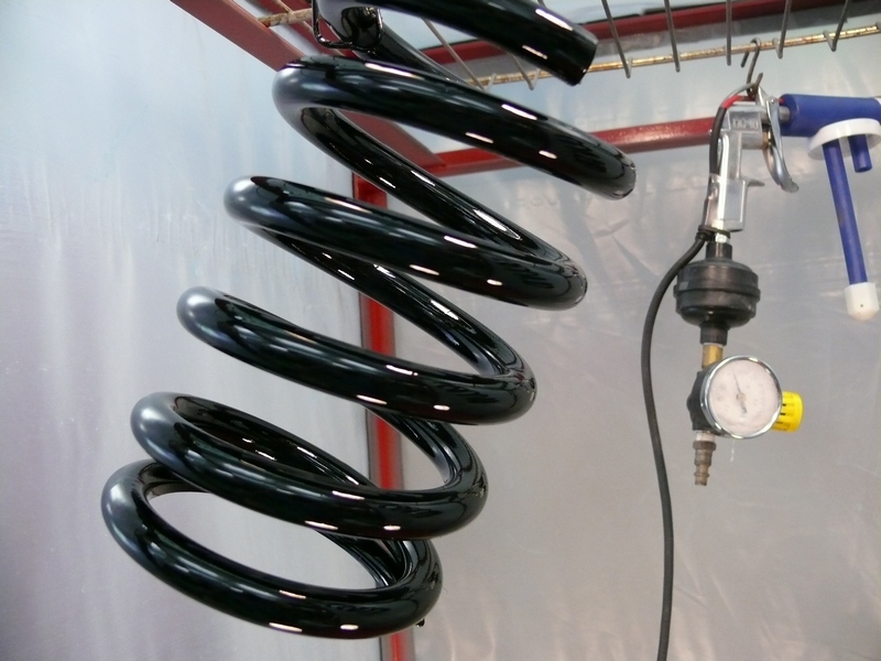 Black coil spring hanging from rack with spray gun and pressure gauge