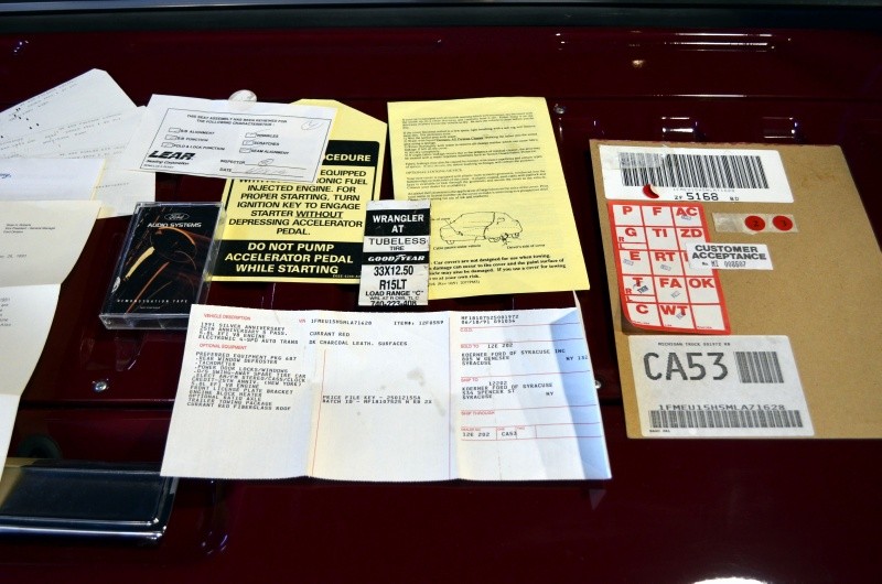 Various vehicle documents, including window sticker and owner's manual pages, spread on a dark red surface