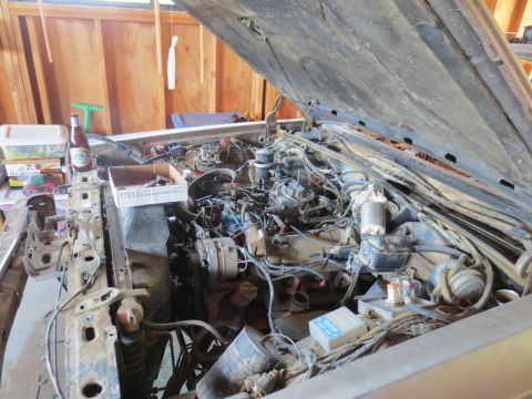 1989 Ford Bronco - The engine bay of a vehicle is shown with many wires and components. A bottle of beer and a box of parts are on the side.