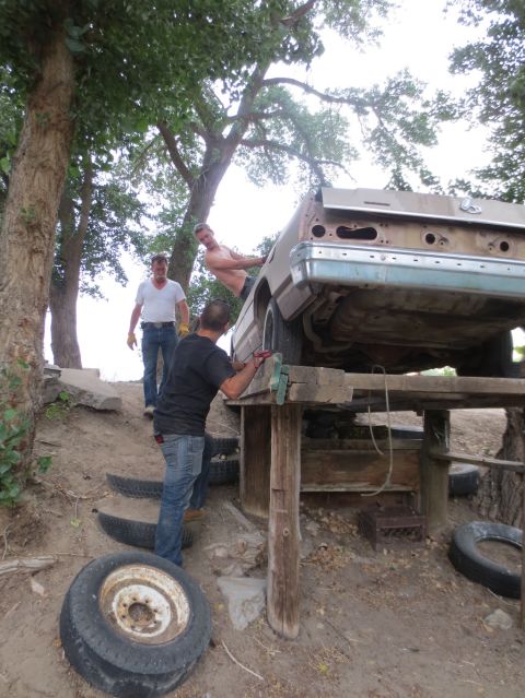 1989 Ford Bronco - Three men are working around the rear of a car body that is elevated on a makeshift wooden platform.