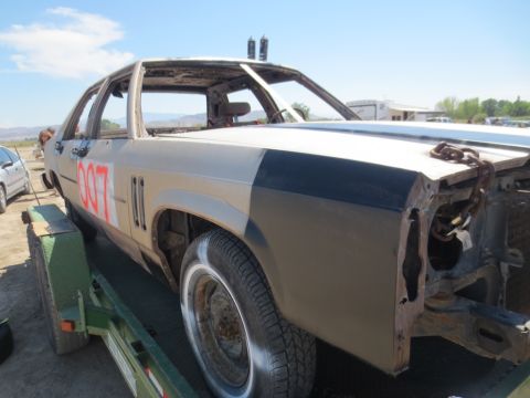 1989 Ford Bronco - Demolished sedan on a trailer, painted tan with a black stripe and red '007' numbers.