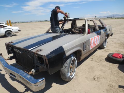 1989 Ford Bronco - A modified sedan, possibly for demolition derby, is being worked on outdoors. A spare tire and gas can sit nearby.
