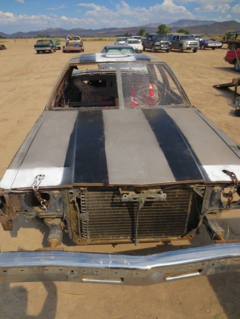 1989 Ford Bronco - A heavily damaged car sits in a dusty lot with other vehicles in the background under a bright sky.