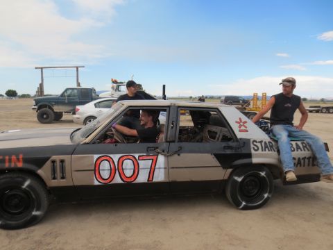 1989 Ford Bronco - A modified sedan, painted with "007" and other markings, sits in a dusty lot with people around it.