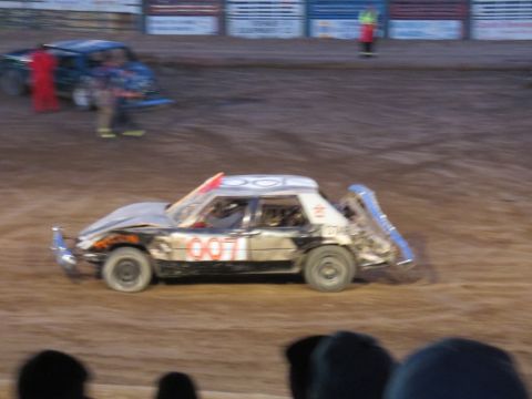 1989 Ford Bronco - A heavily damaged sedan competes in a demolition derby event, with other vehicles visible in the background.