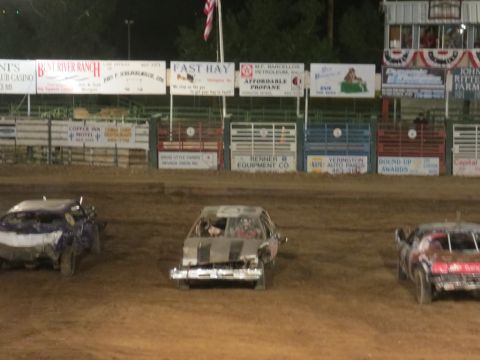 1989 Ford Bronco - Multiple heavily damaged cars are lined up on a dirt track, ready for a demolition derby event.