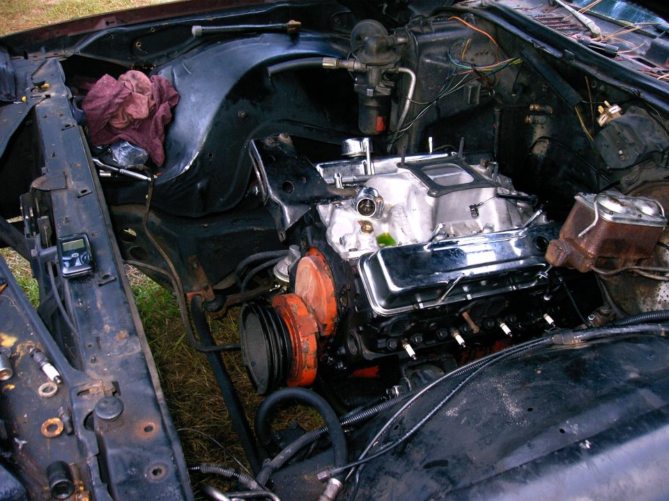 Engine bay with V8 engine, chrome valve covers, and orange pulleys. A digital device is attached to the fender