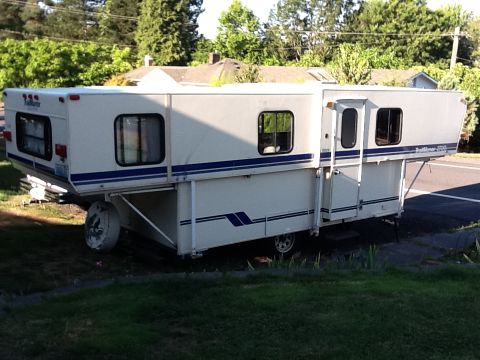 1988 Suzuki Samurai - Slide-in truck camper with blue stripes parked on grass next to a road.