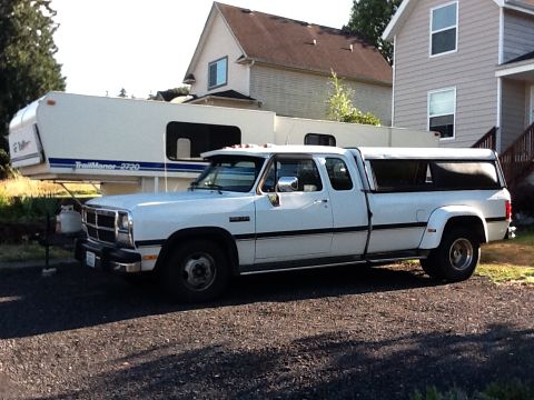 1988 Suzuki Samurai - A white dually pickup truck with a camper shell is parked in front of a house and trailer.