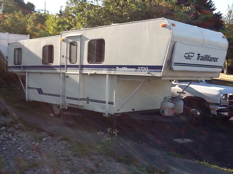 White TrailManor truck camper with blue stripes, mounted on a white truck