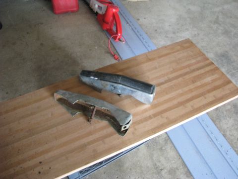 2005 Ford Excursion - Two bumper parts, one chrome and one black, lie on a wooden board next to a red chainsaw.