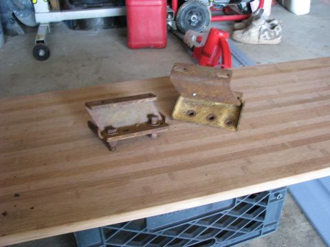 2005 Ford Excursion - Two old, rusted metal brackets sit on a wooden surface in a garage setting.