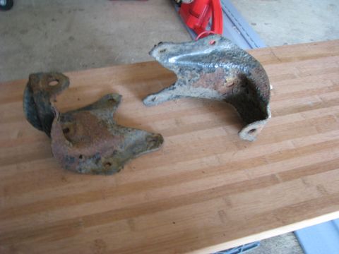 2005 Ford Excursion - Two heavily rusted metal brackets are shown resting on a wooden surface.