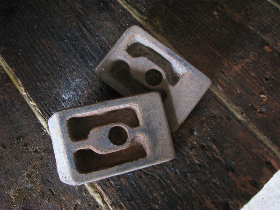 Two metal blocks with rectangular cutouts and a central circular hole, resting on a wooden surface