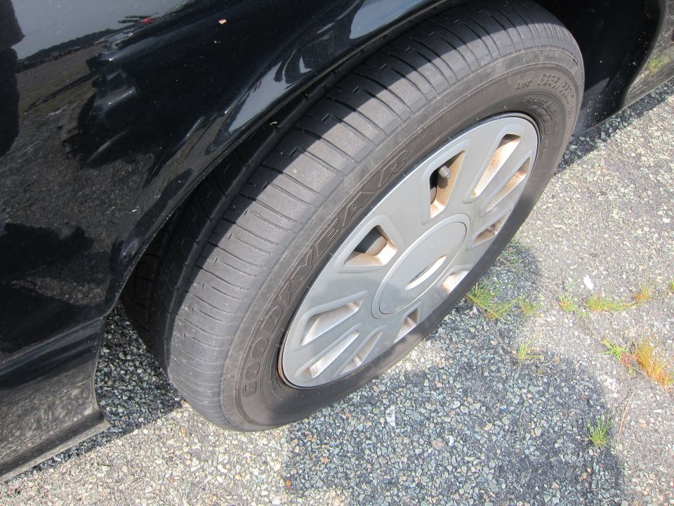 Black car fender and wheel with a silver hubcap on asphalt