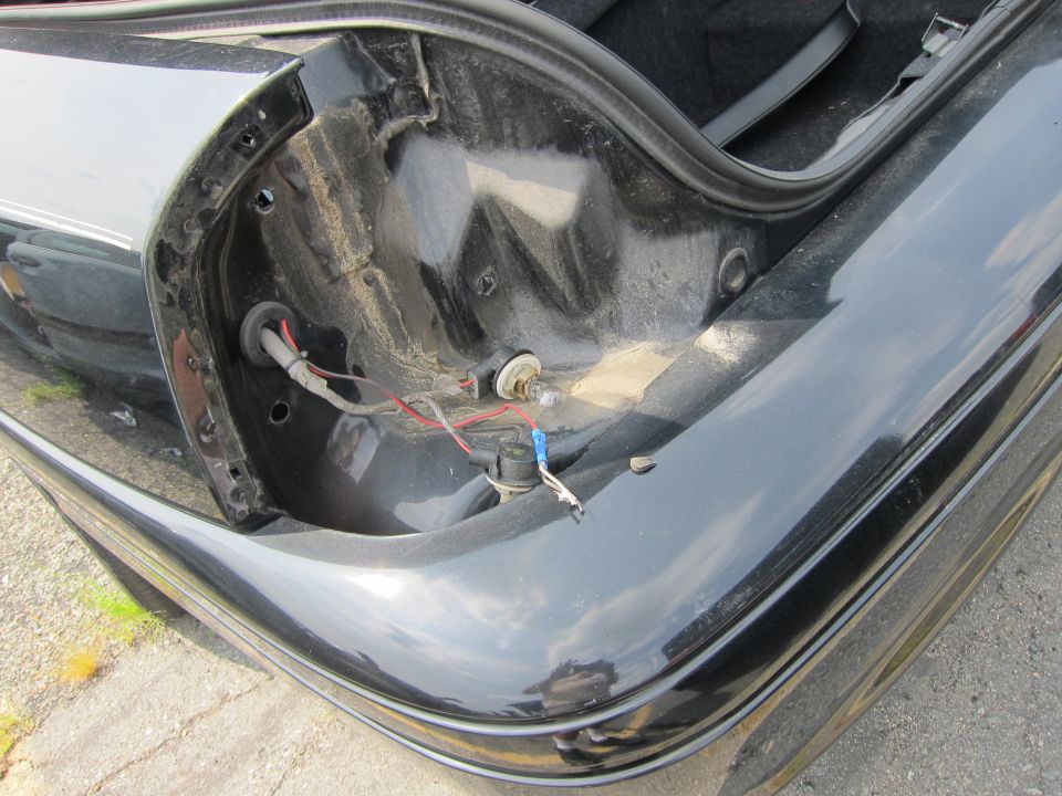 Black car trunk interior showing exposed wiring, a light bulb socket, and the edge of a taillight housing