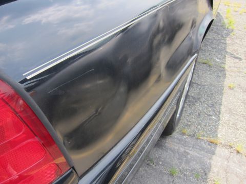 2001 Ford Crown Victoria - The rear quarter panel of a black vehicle shows significant damage and some decorative striping.