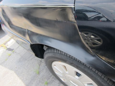 2001 Ford Crown Victoria - A damaged black car's rear quarter panel is shown, with another vehicle reflected in its surface.