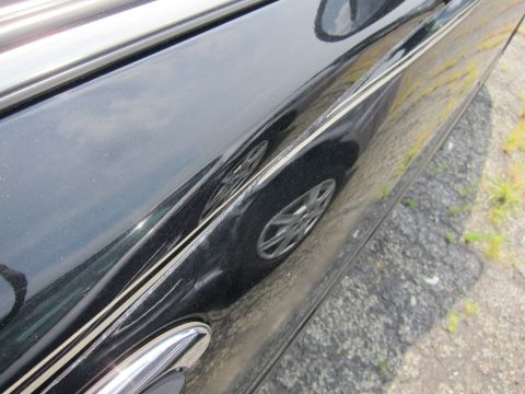 2001 Ford Crown Victoria - A close-up shot of a car's side panel reveals a dent and a decorative pinstripe, with a wheel in view.