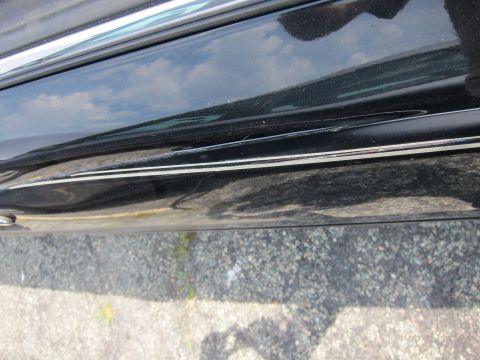 2001 Ford Crown Victoria - Close-up of a black car's side panel, showing damage to the paint and trim.