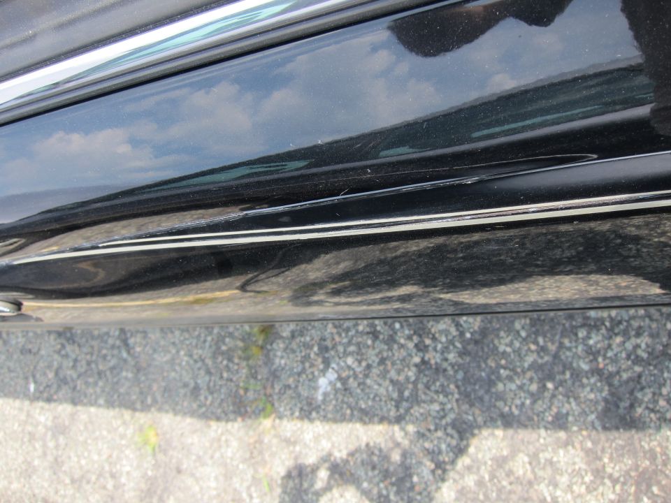 Black car door with chrome trim and visible scratches along the lower body line
