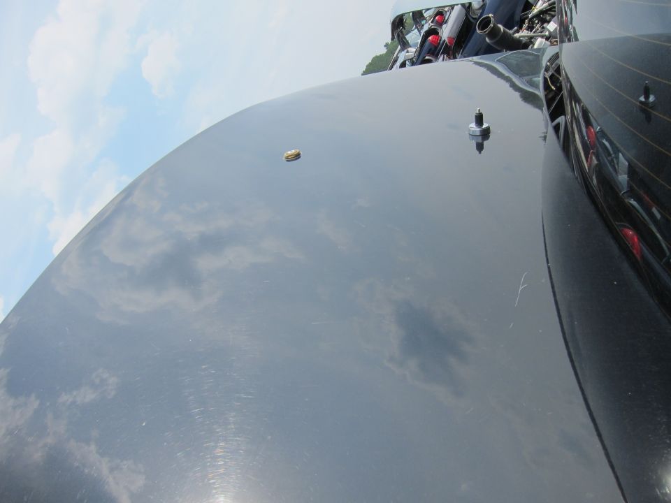 Black car hood with reflections of clouds and a small gold emblem