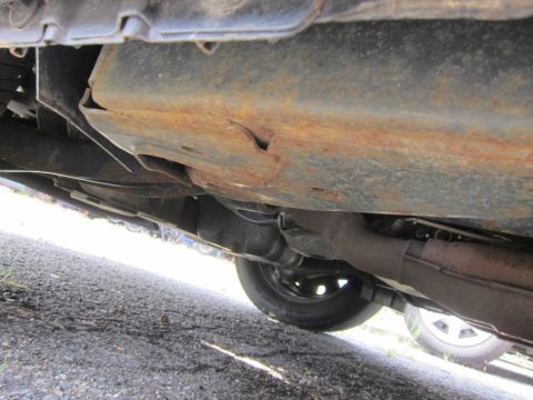 2001 Ford Crown Victoria - Undercarriage view reveals rusty metal and exhaust system components, with a tire visible.