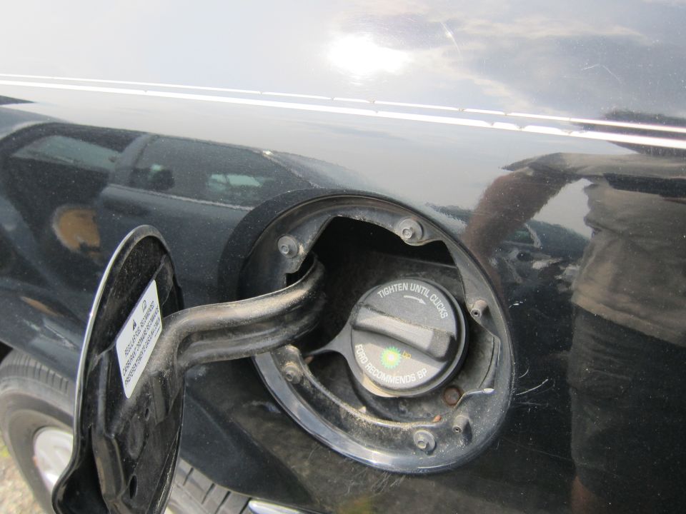 Close-up of a black car's open fuel filler door and cap, showing text instructions