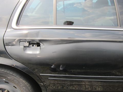 2001 Ford Crown Victoria - The rear door of a black sedan shows damage and a missing door handle.