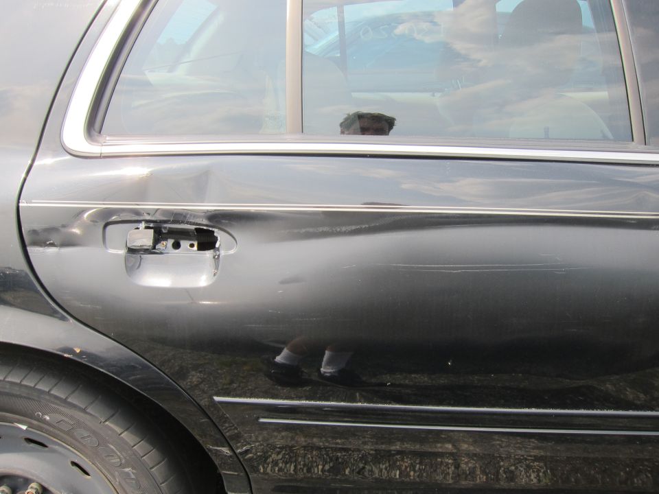 Side of a black sedan with a missing door handle and damage to the rear door