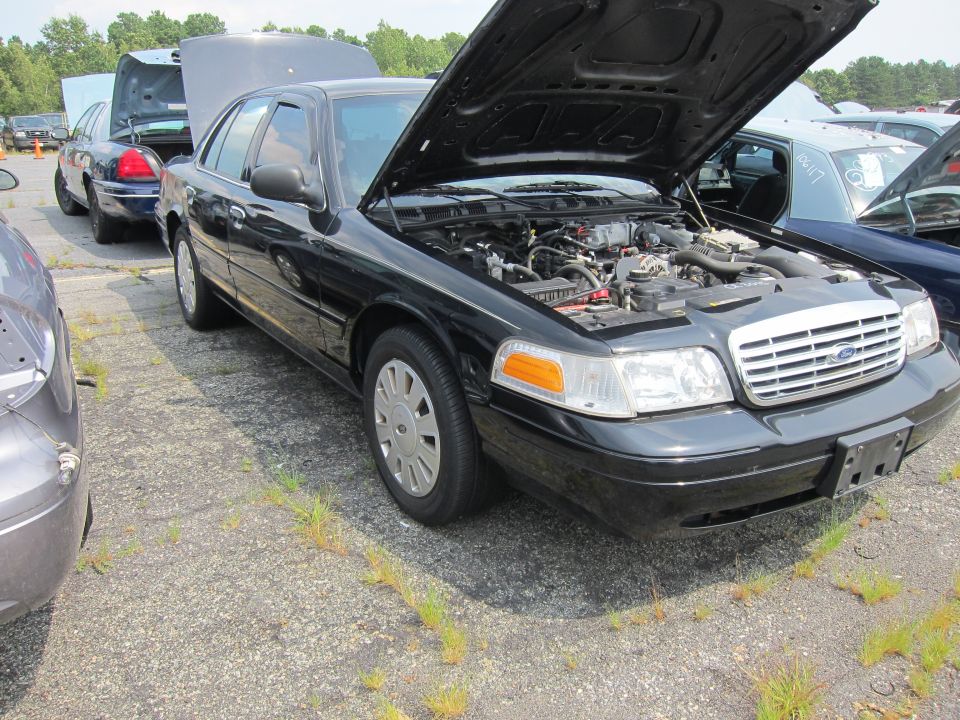 Black 2001 Ford Crown Victoria with hood open, parked on gravel lot
