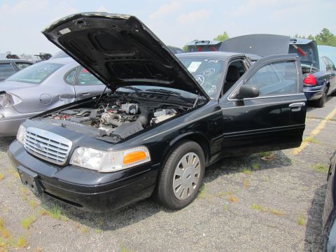 2001 Ford Crown Victoria - A black 2001 Ford Crown Victoria is parked with its hood and driver's door open, revealing the engine compartment.