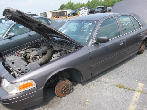 2001 Ford Crown Victoria - This 2001 Ford Crown Victoria is missing its wheels and has its hood open, likely at a junkyard.