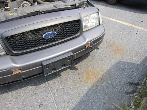 2001 Ford Crown Victoria - The front of a gray 2001 Ford Crown Victoria shows damage to the bumper and an open hood.