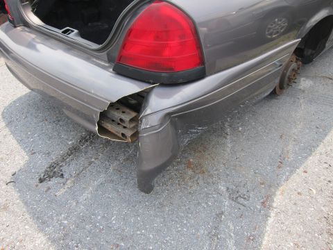 2001 Ford Crown Victoria - The rear bumper of a 2001 Ford Crown Victoria is heavily damaged, revealing its internal frame and missing a rear wheel.