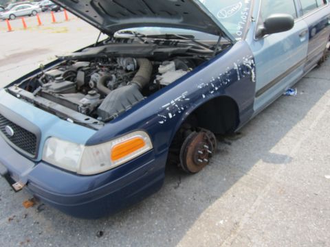2001 Ford Crown Victoria - This Ford Crown Victoria is missing a front wheel and has its hood open, revealing the engine compartment.
