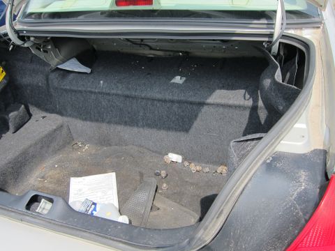 2001 Ford Crown Victoria - The trunk of a car is open, revealing a dusty interior with scattered hardware and a piece of paper.