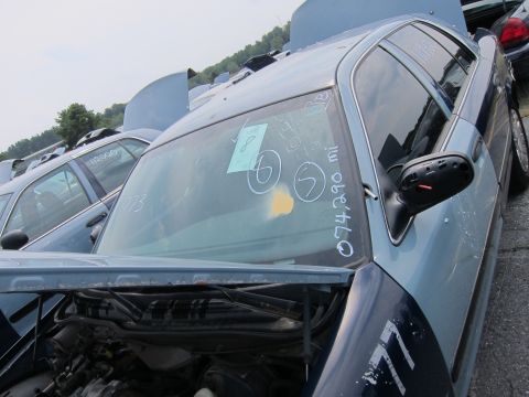 2001 Ford Crown Victoria - A blue 2001 Ford Crown Victoria sits in a junkyard with its hood open, displaying various markings on the windshield.