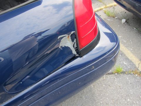 2001 Ford Crown Victoria - The rear quarter panel of a blue sedan exhibits significant damage and peeling paint, revealing rust underneath.