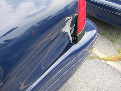 2001 Ford Crown Victoria - A damaged blue car's rear quarter panel shows extensive damage and peeling paint, with another vehicle partially visible.