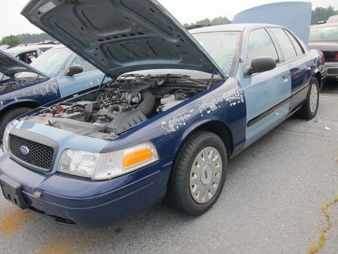2001 Ford Crown Victoria - A blue Ford Crown Victoria with its hood and trunk open is parked in a lot with other vehicles.