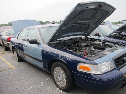 2001 Ford Crown Victoria - Two-tone Ford Crown Victoria police car with hood open, parked in a lot with other vehicles.