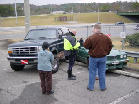 1995 Ford Bronco - A dark green Ford Bronco is parked next to a green BMW that has driven onto a curb, with several people observing.