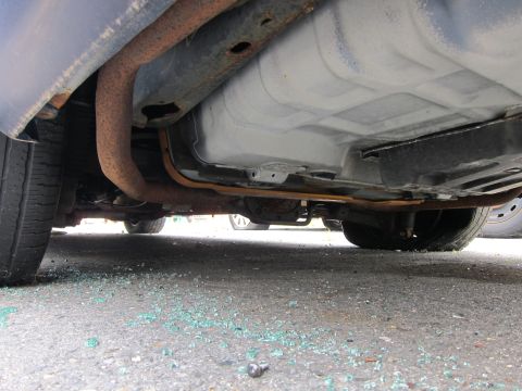 2001 Ford Crown Victoria - Broken glass litters the ground beneath the rusty undercarriage of a vehicle.