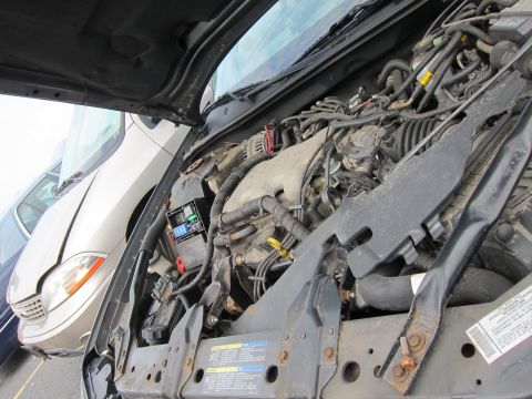 2001 Ford Crown Victoria - The engine bay of a car is shown, with a fuse box prominently displayed. Another vehicle is partially visible in the background.