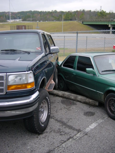 1995 Ford Bronco - A dark green 1995 Ford Bronco is parked close to a green sedan, with the front of the Bronco dominating the frame.