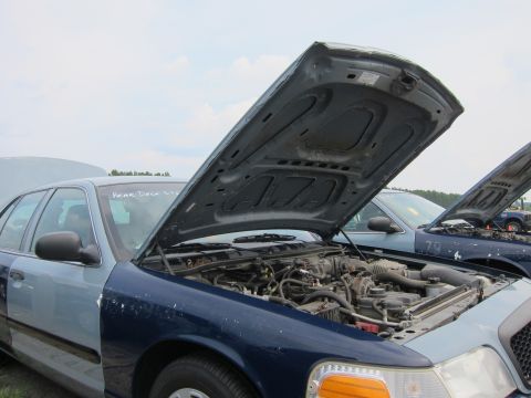 2001 Ford Crown Victoria - Two Ford Crown Victorias are parked outside with their hoods open, revealing their engines under a cloudy sky.